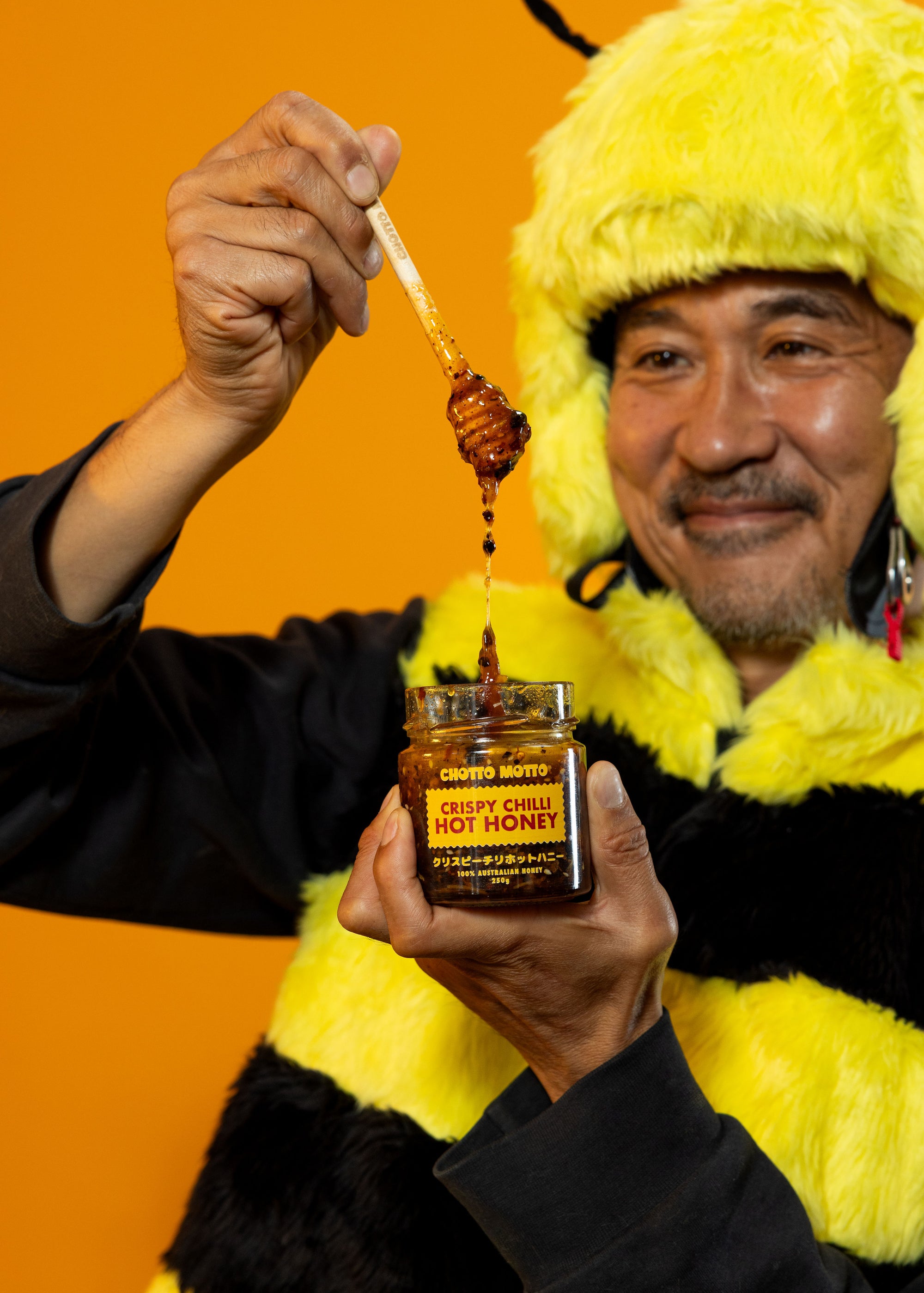 Person in a bee costum with a jar of Crispy Chili Honey against an orange background