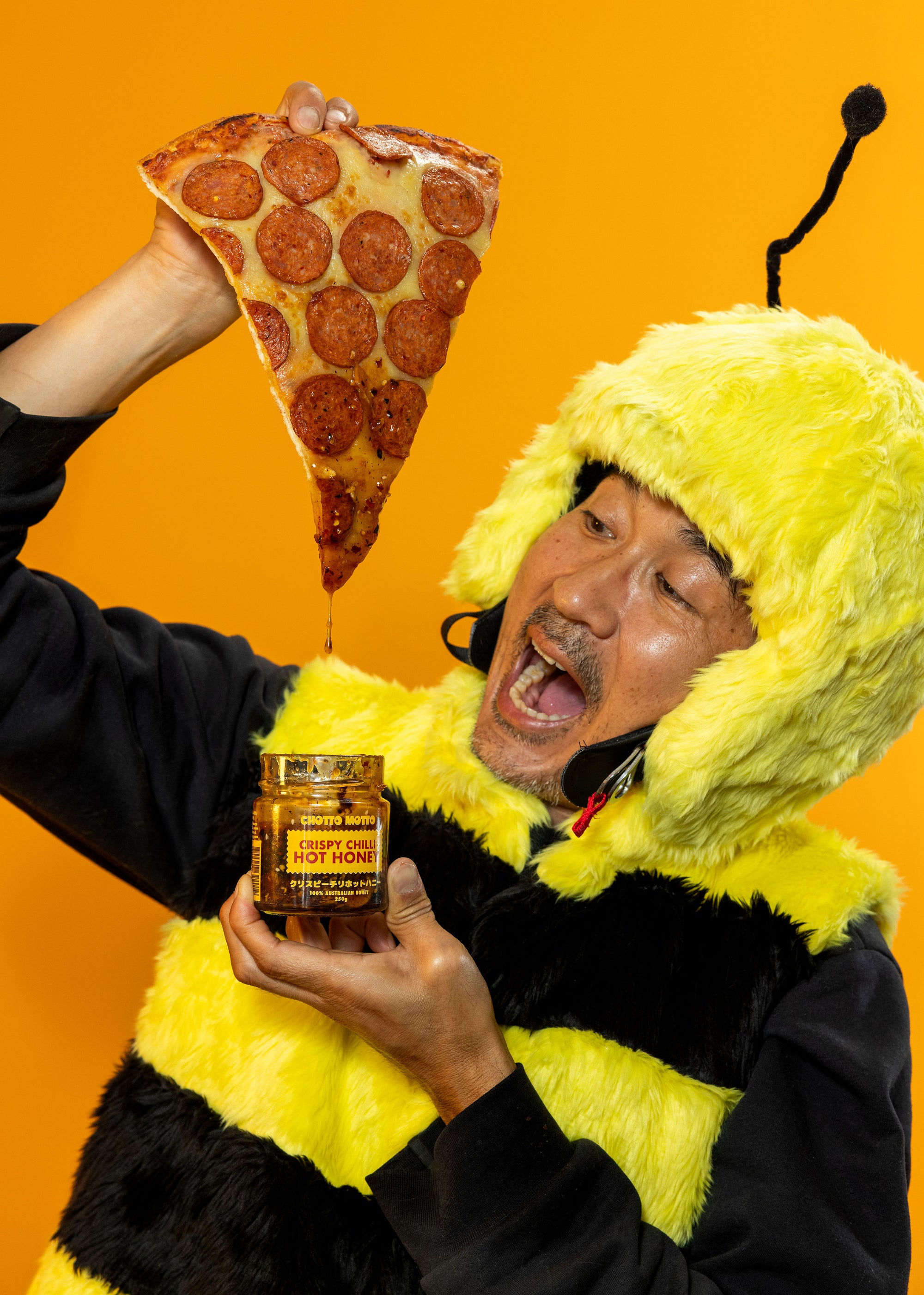 Person in a bee costume dipping pizza into a jar of Crispy Chilli Hot Honey