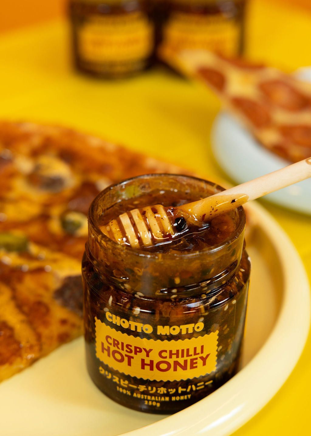 Jar of Chotto Motto Crispy Chilli Hot Honey with a wooden dipper
